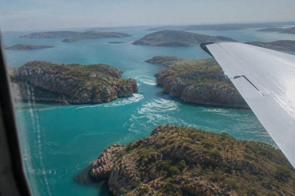 A light aircraft wing above scattered green islands and turquoise reefs of the Buccaneer Archipelago
