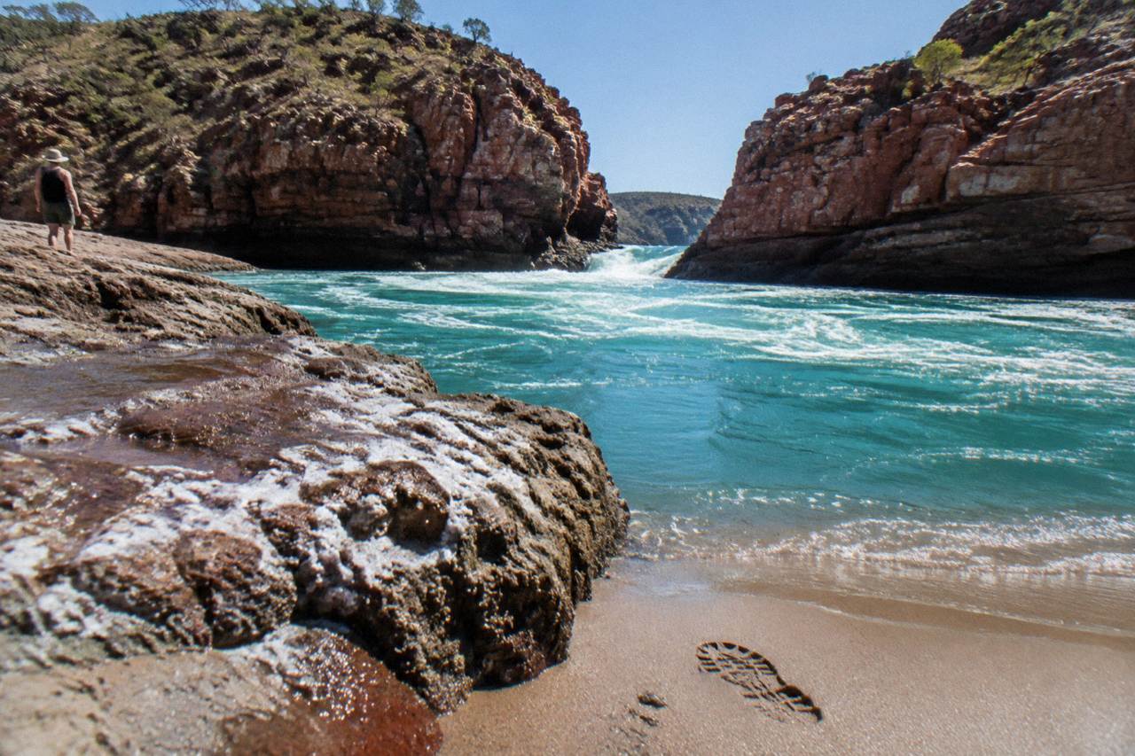 Turquoise tidal water rushing through a narrow red rock gap in Talbot Bay under a clear sky