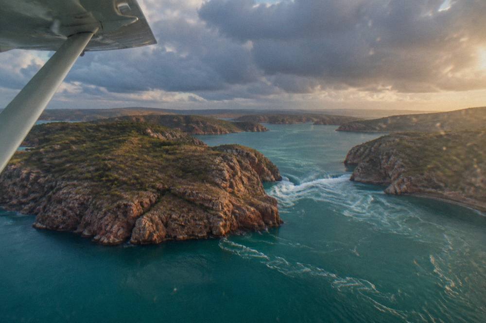 A light aircraft flying low over turquoise water dotted with rugged rocky islands