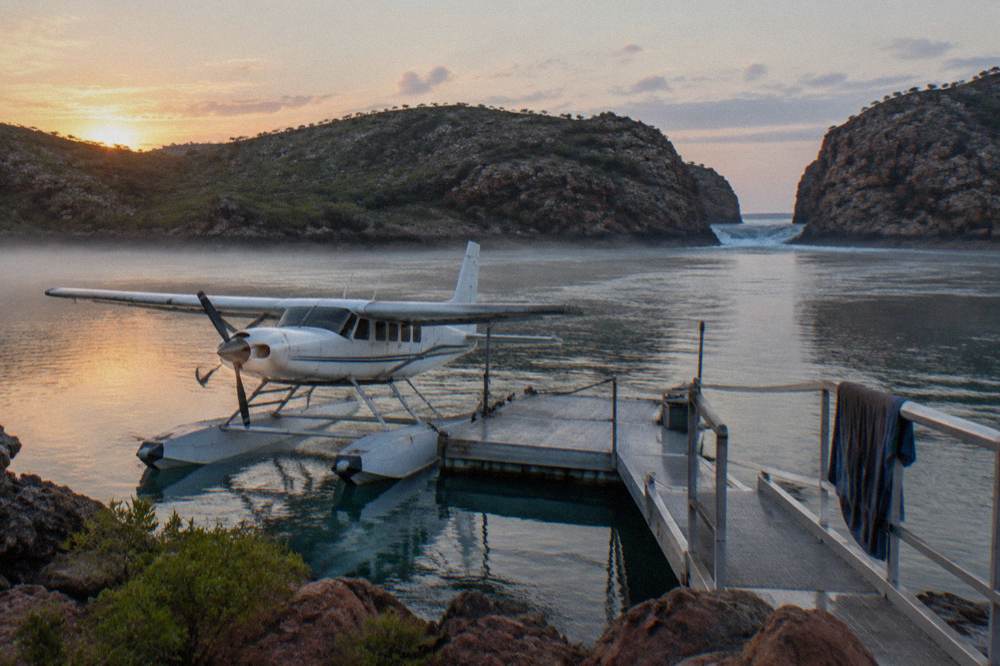 A seaplane moored beside a floating pontoon in a remote bay surrounded by rocky islands