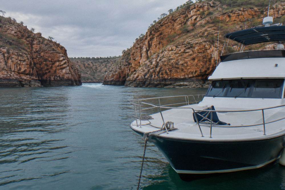 A cruise boat anchored near red cliffs on a remote Kimberley shoreline