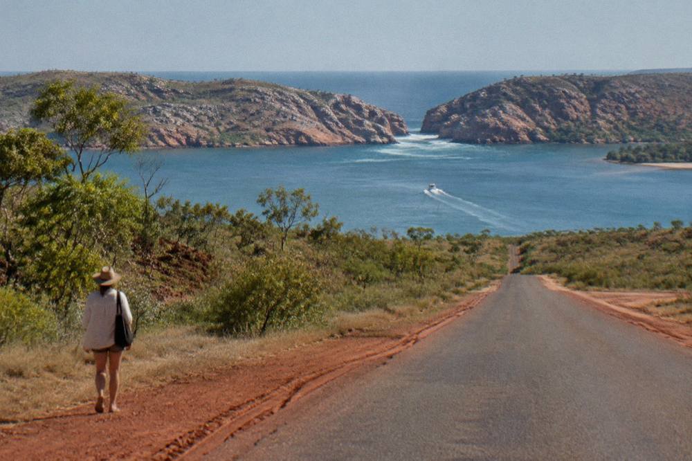 A sealed red-dirt road running north through scrub toward a distant coastline