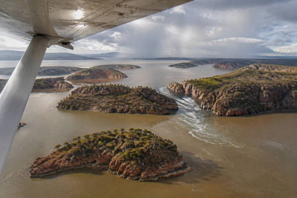 A light aircraft flying low over turquoise island-dotted water in the Kimberley