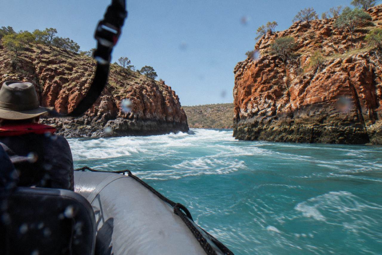 Turquoise tidal water rushing through a narrow red rock gorge in a remote Kimberley bay