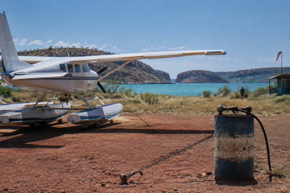 A light aircraft on a red dirt airstrip beside turquoise water in the Kimberley at midday