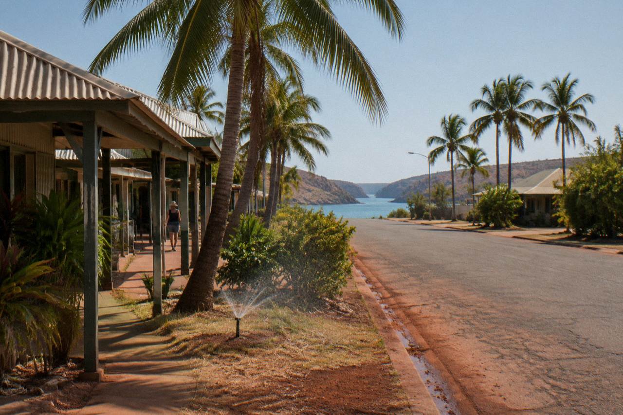 A quiet street in Broome under red pindan soil and green coconut palms on a clear dry season morning