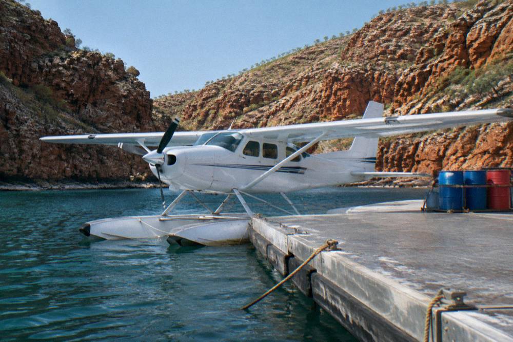 Seaplane moored beside a floating pontoon in a remote bay surrounded by red rock