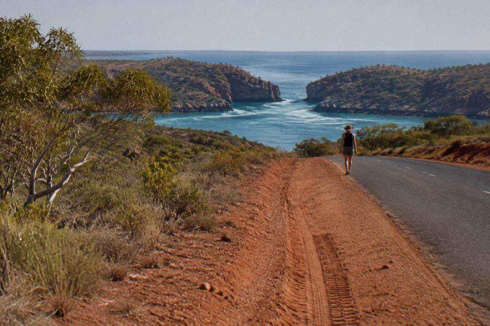 Sealed outback road running north through red dirt country toward a distant coastline