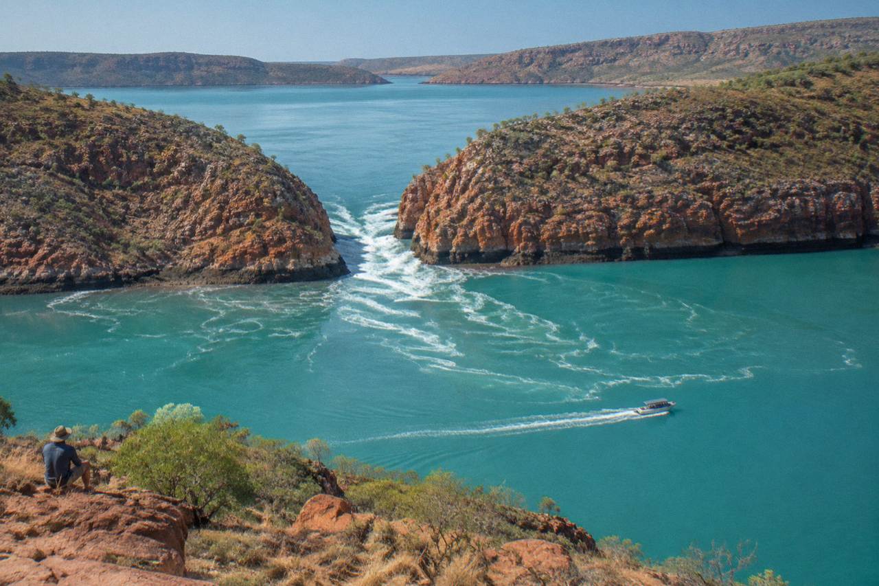 Aerial view of turquoise water rushing through two narrow coastal gaps in a red rocky range
