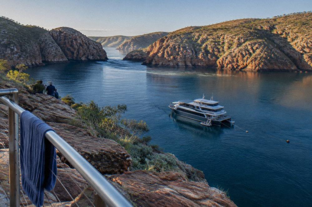 A passenger cruise vessel moored in calm blue water beside red rock cliffs