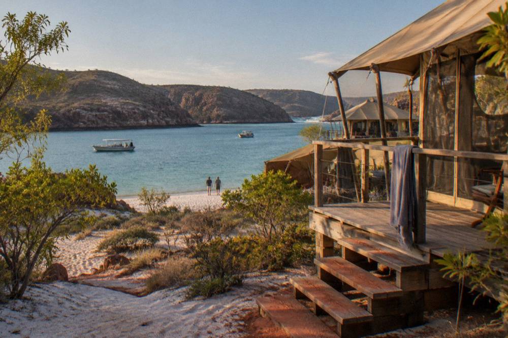 Safari tents pitched on white sand overlooking turquoise water at a pearl farm bay