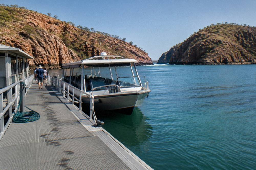A small cruise boat moored beside a floating pontoon in a sheltered Kimberley bay