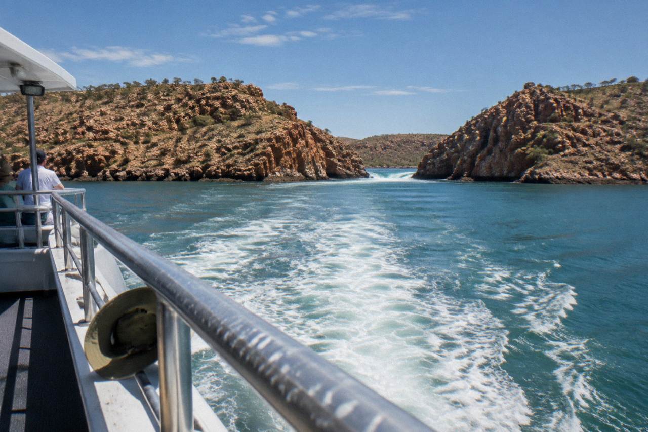 A cruise vessel cruising through red rock islands in Talbot Bay under a wide blue sky