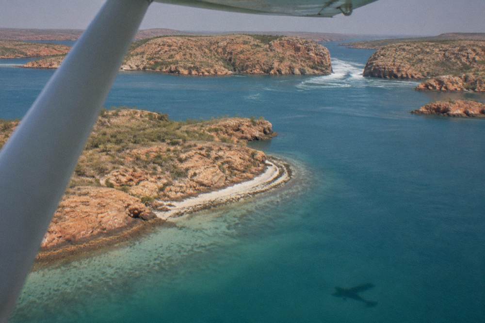 A small plane flying over turquoise water dotted with rugged islands