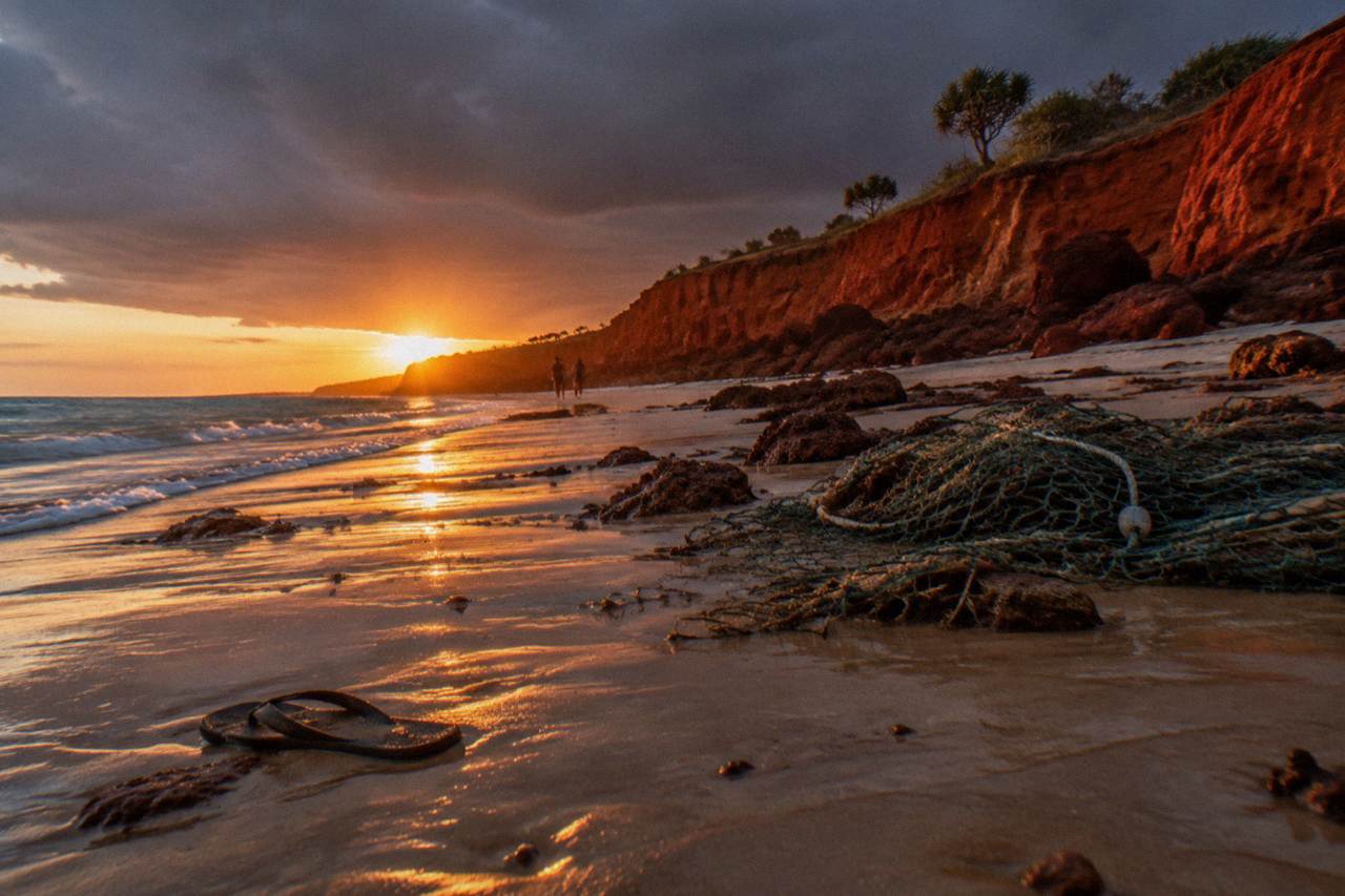 Red pindan cliffs along a wide sandy beach at sunset in Australia's northwest