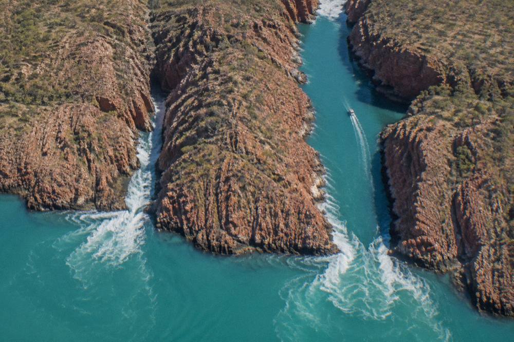 Aerial view of two parallel narrow channels cutting through red cliffs above turquoise sea