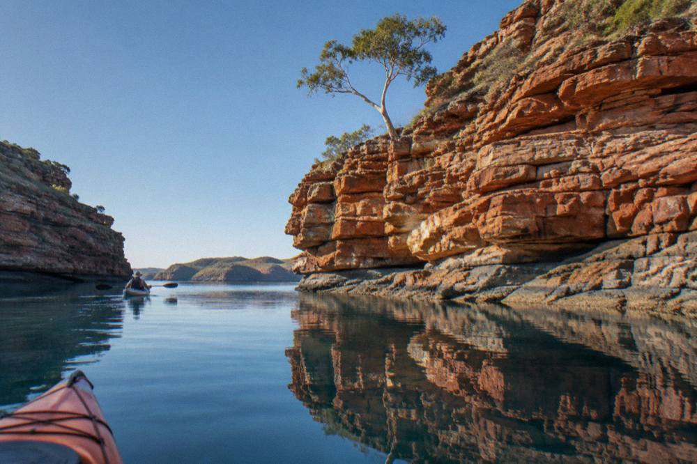 Red sandstone cliffs of the Buccaneer Archipelago reflected in calm water under a clear dry season sky