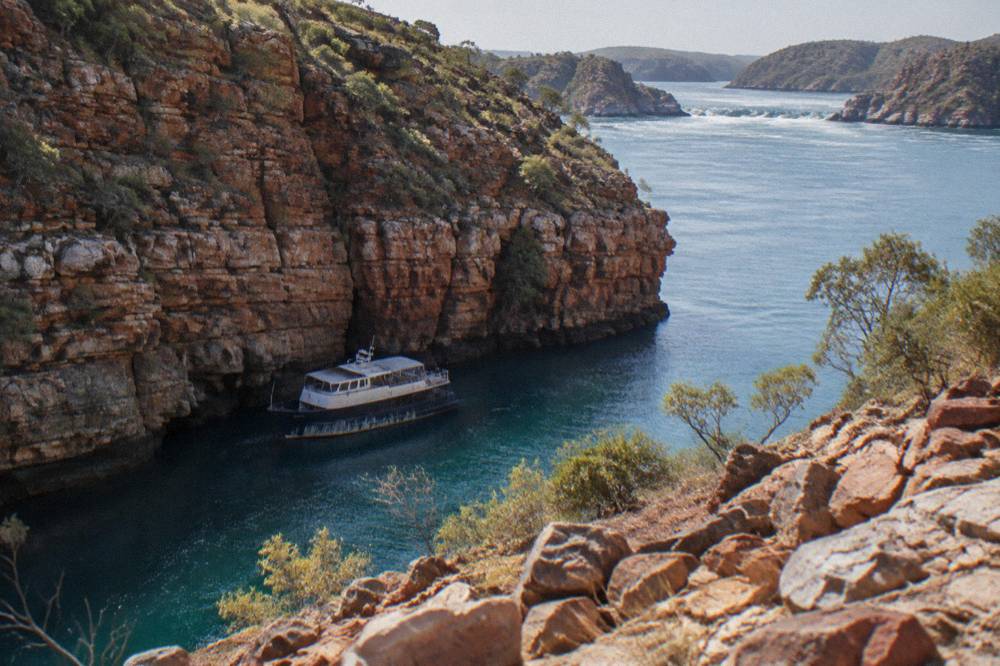 Small cruise boat passing close to steep layered rock walls along a Kimberley inlet