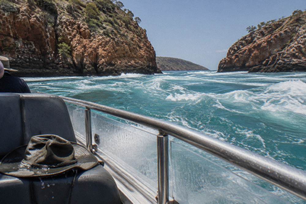 Turbulent water rushing through a narrow rocky channel between red cliffs at Horizontal Falls