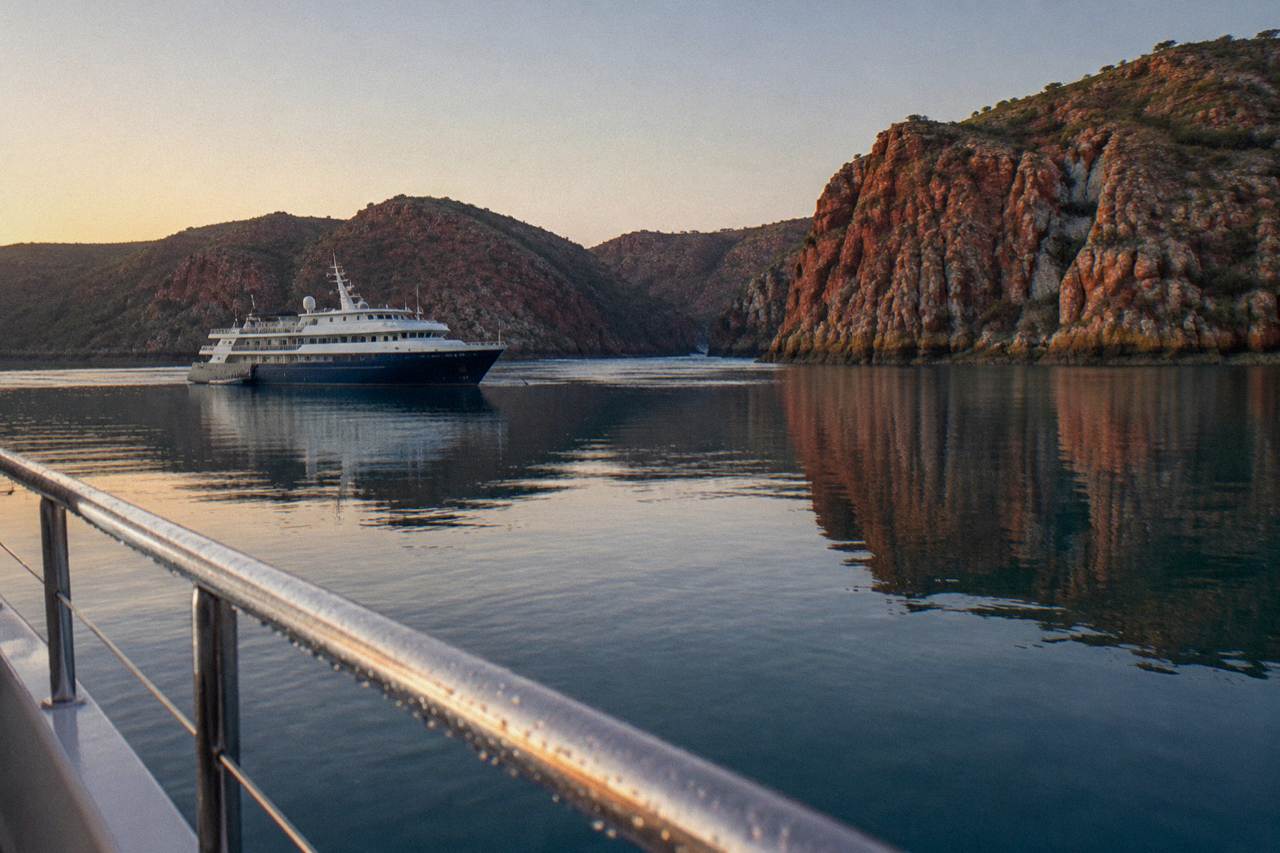 Expedition cruise vessel anchored near red cliff coastline in Talbot Bay at sunrise