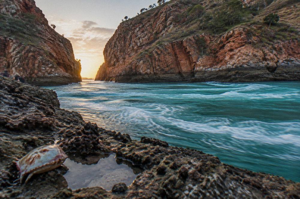 Turquoise water rushing through a narrow rocky gap between red cliff walls