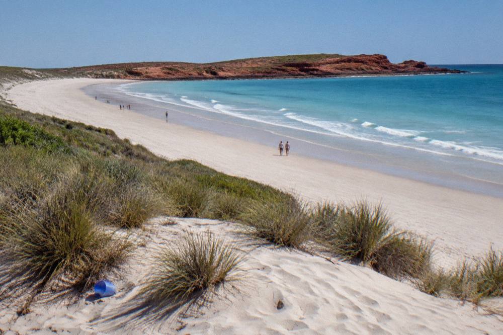 Wide white sand beach curving toward red rock headland under a clear tropical sky