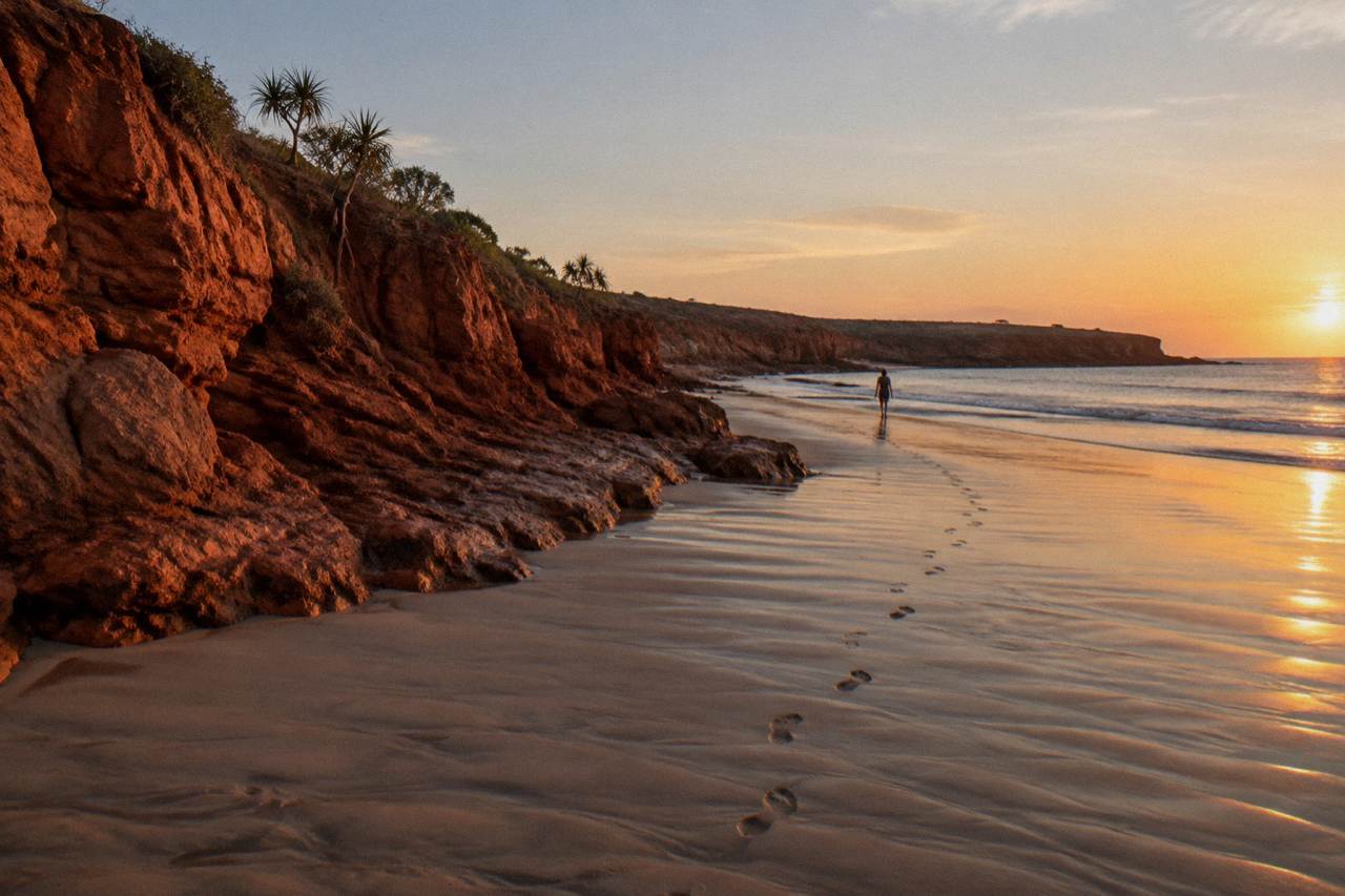 Red pindan cliffs along Cable Beach at sunset with smooth sand running to the waterline