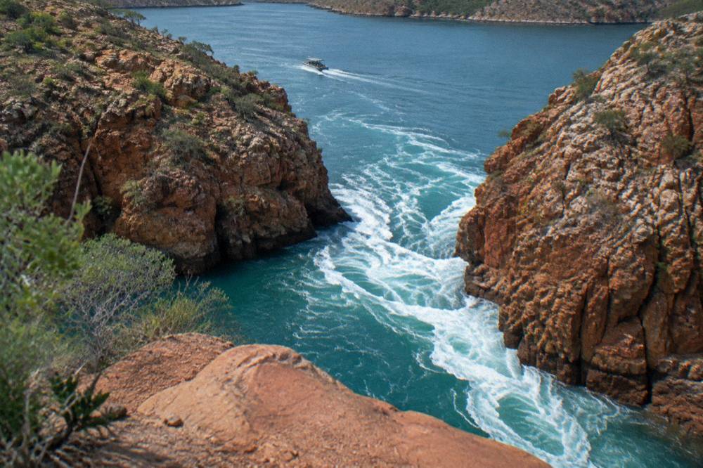 White water rushing through a narrow gap between red rock walls from above