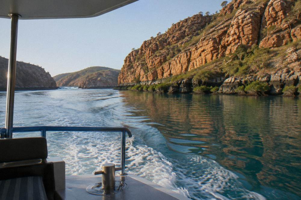 A boat cruising near red cliffs above clear tropical water