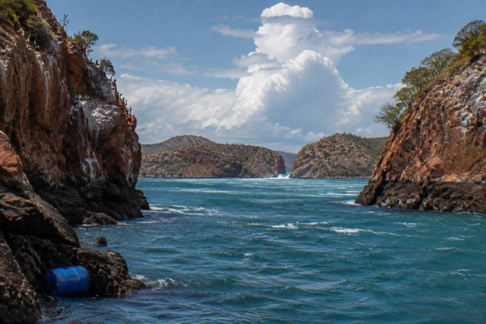 Red sandstone cliffs of the Buccaneer Archipelago rising from clear blue sea under scattered clouds