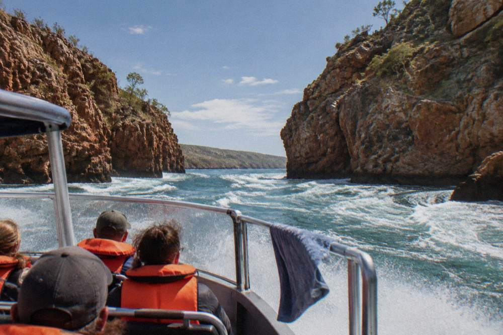 A small boat cutting through white turbulent water between steep rock walls
