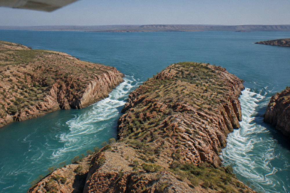 Aerial view of two narrow channels cutting through a red rock range with turbulent whitewater