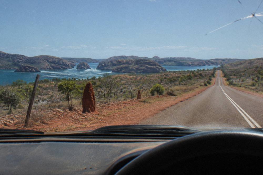 A sealed outback highway stretching straight toward the horizon through red dirt and low scrub