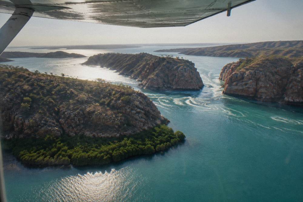 A fixed-wing light aircraft wing above turquoise water and rocky islands of the Buccaneer Archipelago