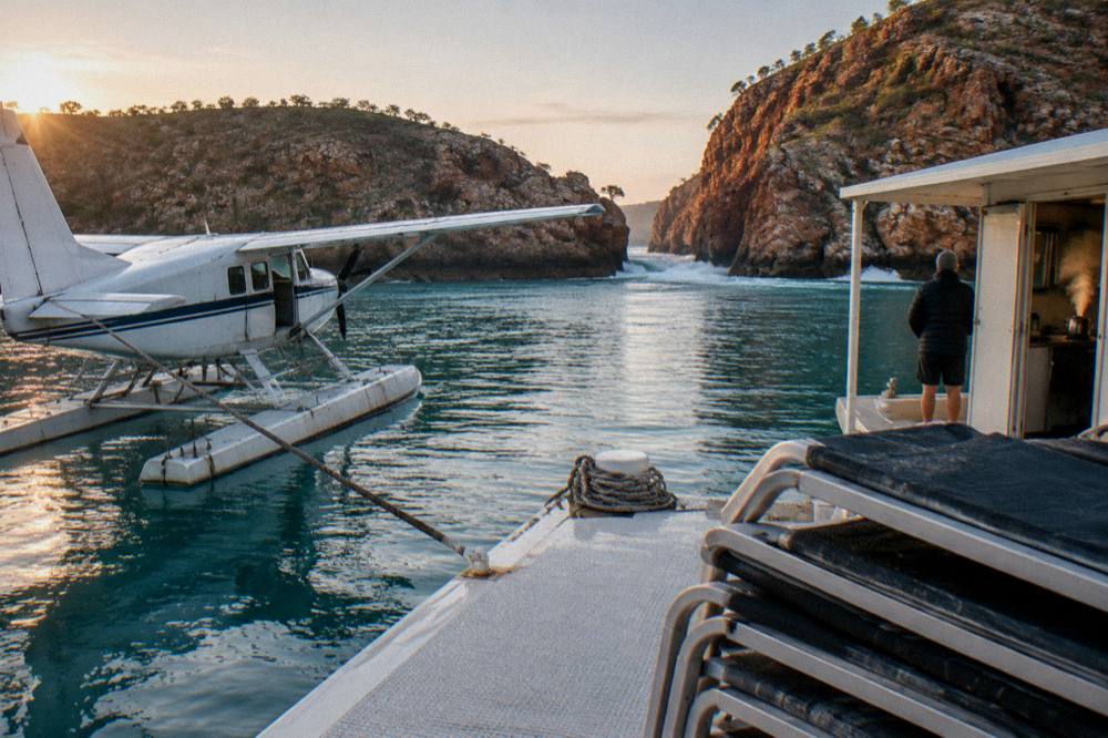 A pontoon seaplane base on turquoise water beside rocky cliffs at sunrise