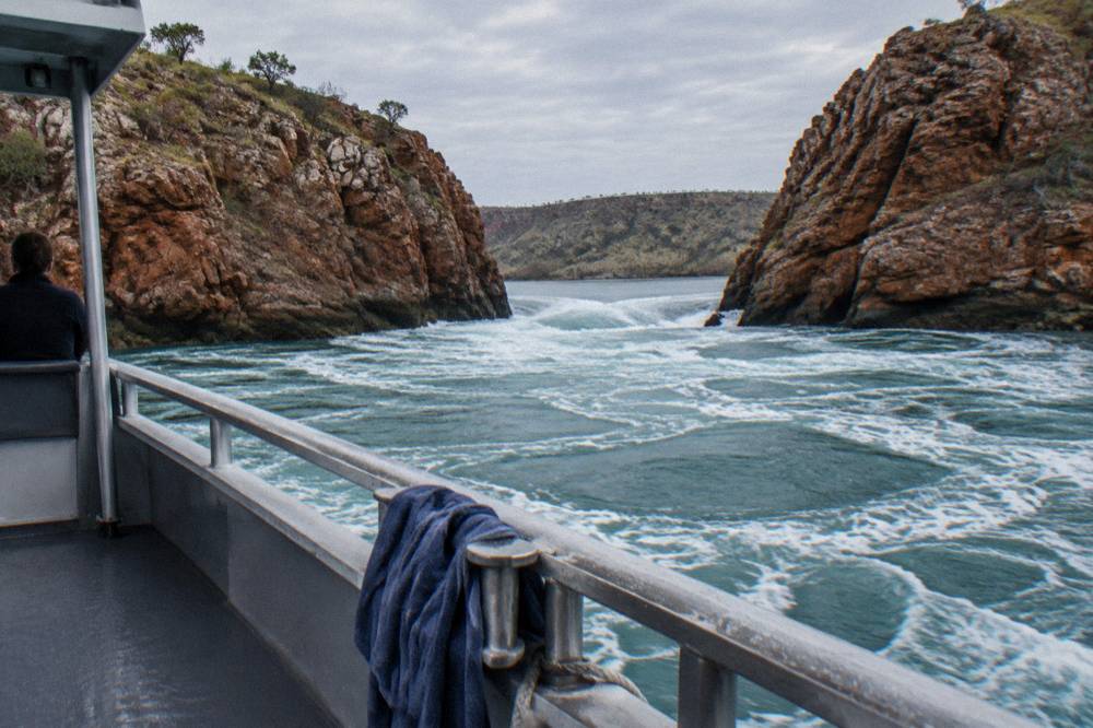 A tidal channel between red rock islands with white water rushing through a narrow gap
