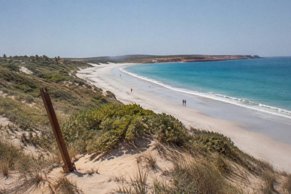 Long white sand beach curving toward a headland under a wide sky
