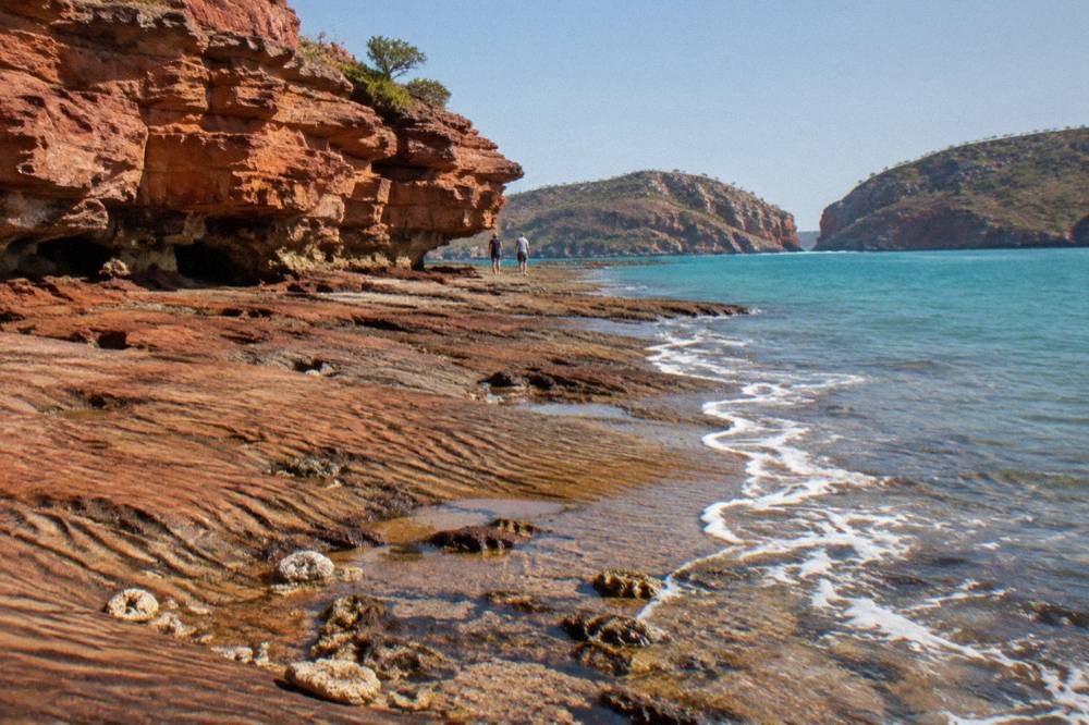 Red sandstone cliffs meeting turquoise water at a rocky point