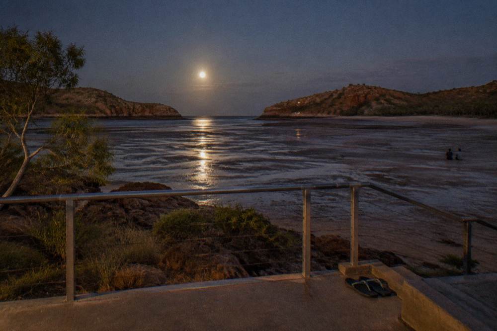 Moonlight reflecting across wet tidal flats toward a shoreline