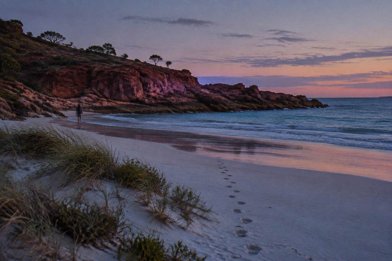 White sand beach with red rock headland at sunset