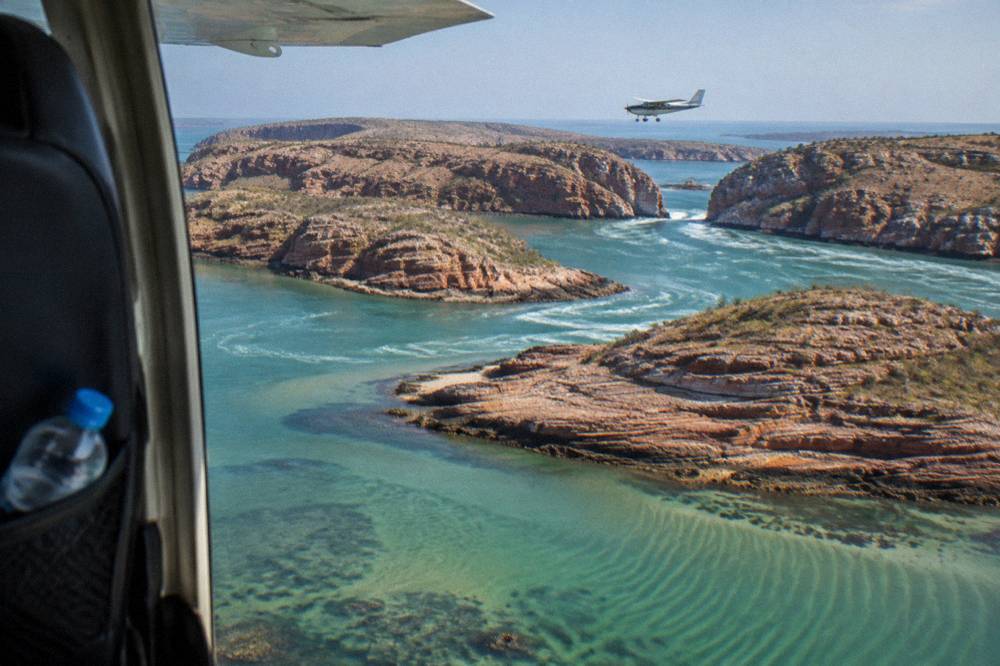 A light aircraft flying low over striped rock islands and clear sea
