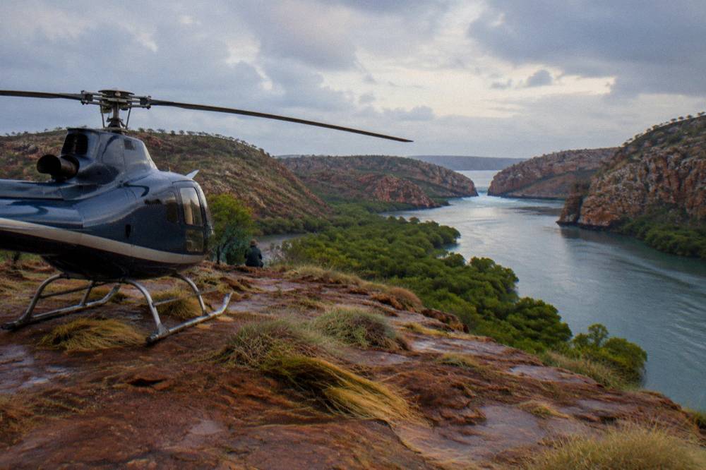A helicopter parked on a red cliff above a winding river gorge