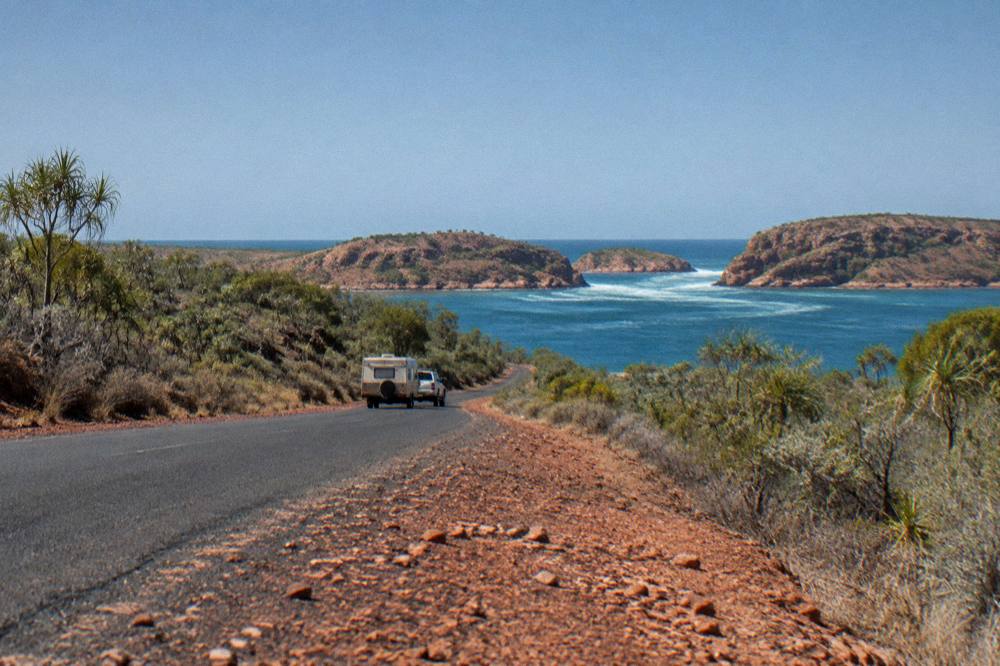 A caravan and four wheel drive on a sealed road through red pindan country