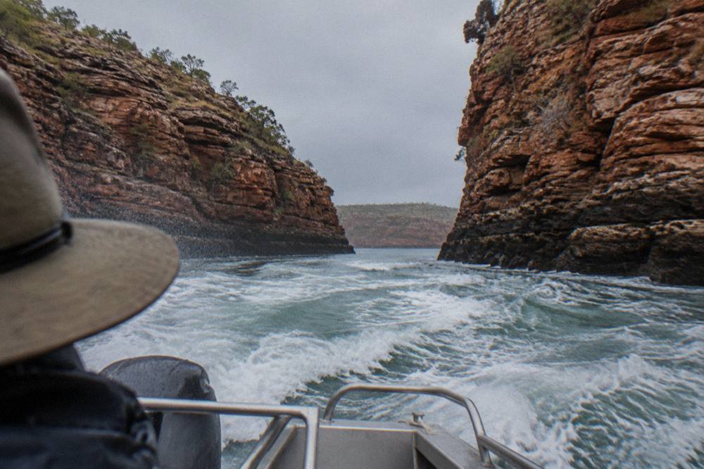 A power boat cutting across white turbulent water between towering red cliff walls