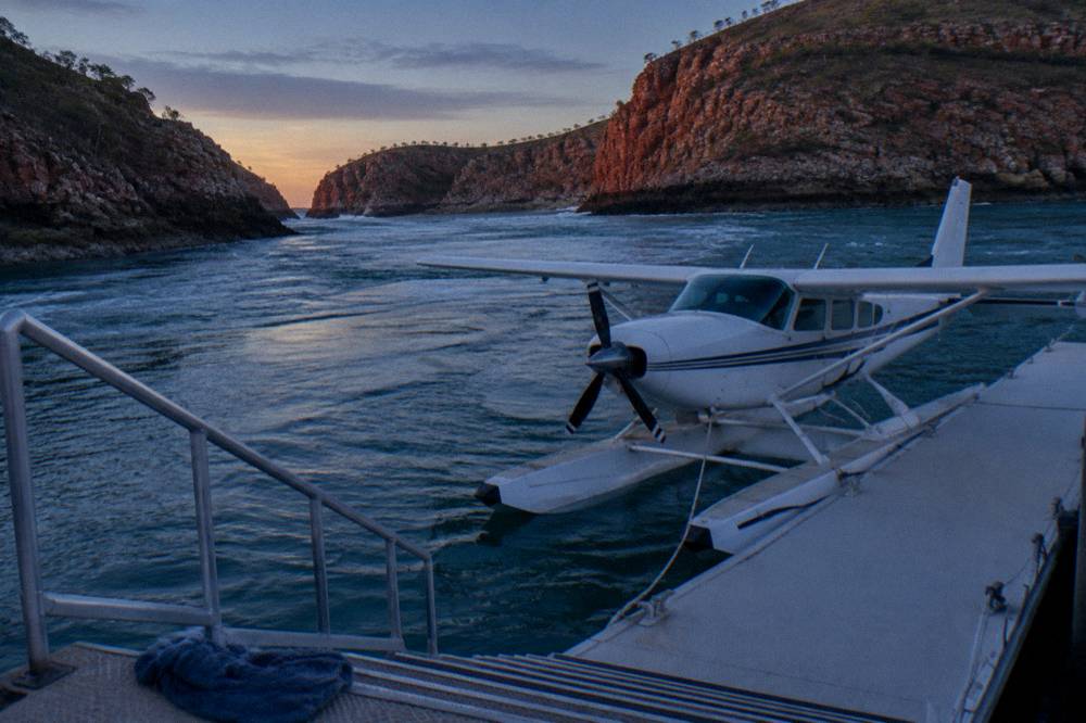 A seaplane moored beside a floating pontoon in a remote bay ringed by rocky islands
