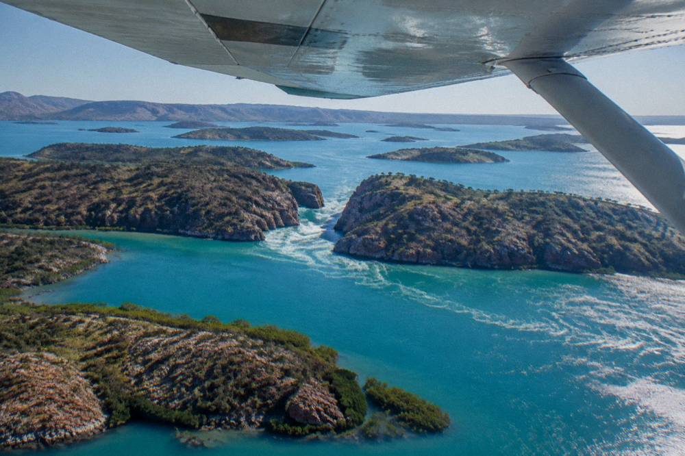 A light aircraft wing above scattered green islands in bright blue sea