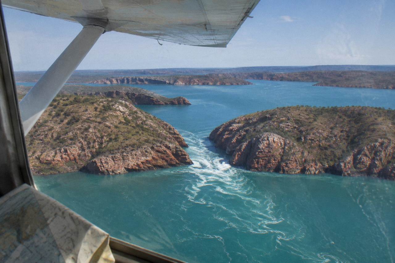A light aircraft flying over red rocky islands and turquoise water in the Buccaneer Archipelago