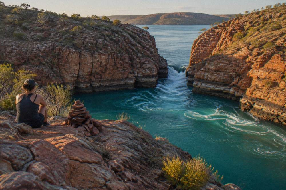 Turquoise water rushing through a narrow gap between layered red rock walls