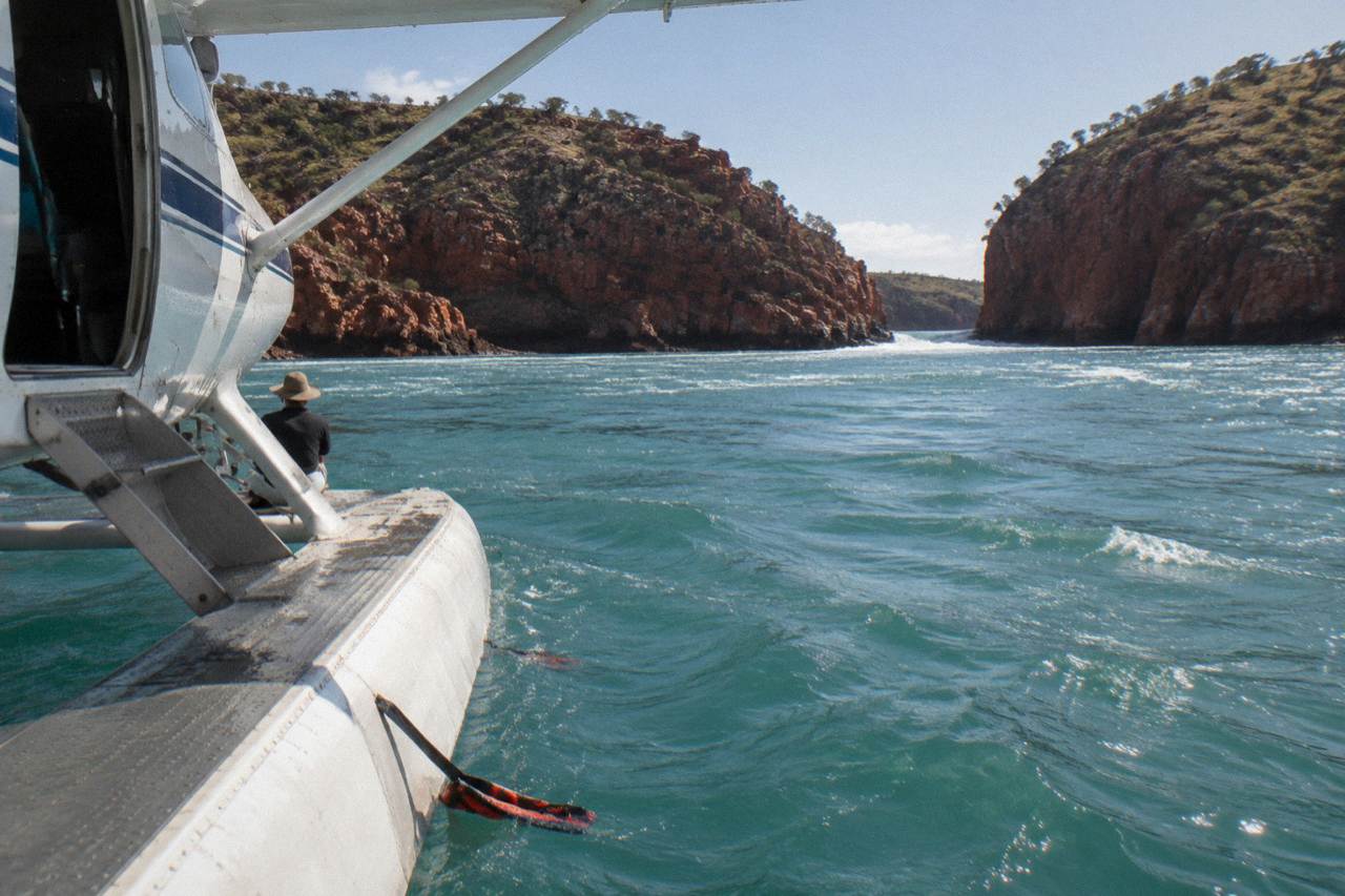 A seaplane resting on calm turquoise water beside a red rock gorge in the Kimberley