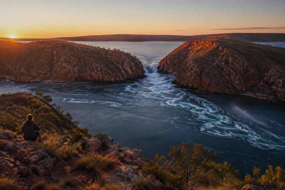 Aerial view of white water streaming through a gap between red rock headlands